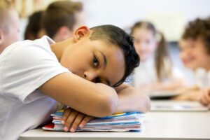 Boy with his head on a desk looking sad.